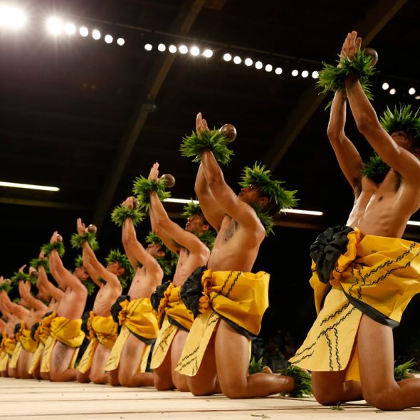 Men’s hula group performing on their knees at Merrie Monarch Festival, chanting with uplifted hands toward the sky in a powerful expression of Hawaiian spirituality and tradition.